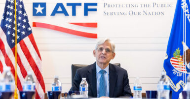 Then-U.S. Attorney General Merrick Garland in a dark suit and blue tie sitting at a conference table at the ATF with an ATF logo on the wall in back of him