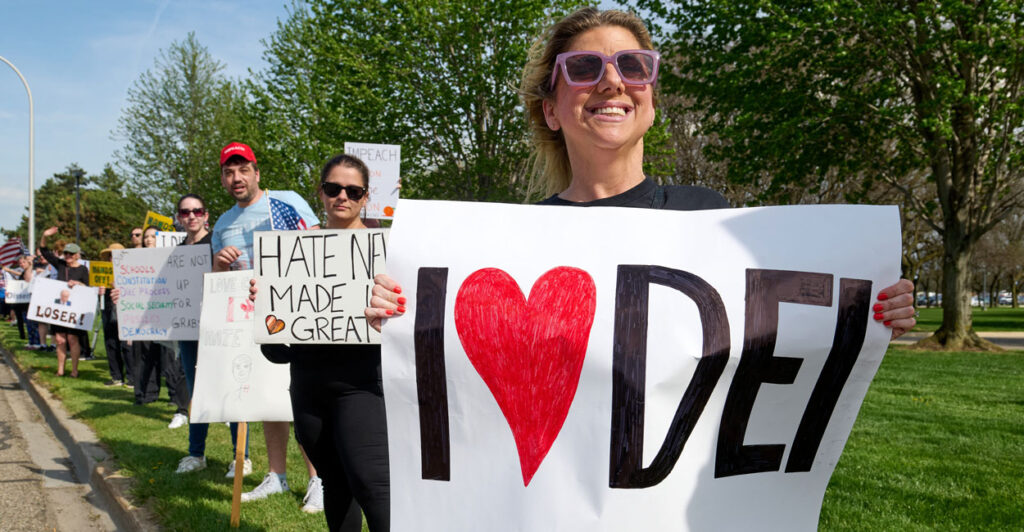 protesters line the street holding signs, with the protester in front holding a sign that says I love DEI