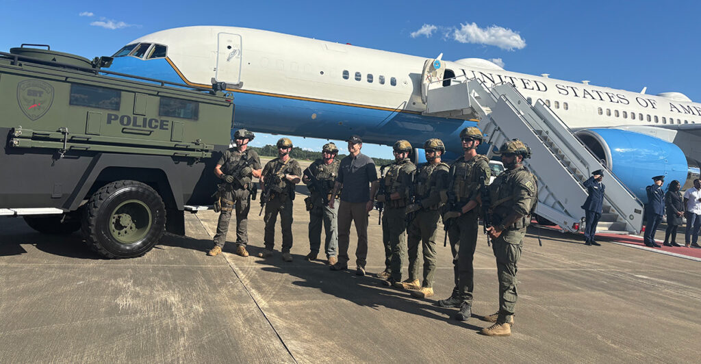 Secretary of Defense Pete Hegseth poses with Fort Bragg police in Fayetteville, North Carolina, with his aircraft as backdrop.