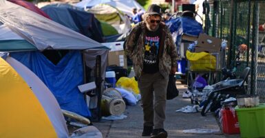 A homeless man walks down the sidewalk surrounded by tents.