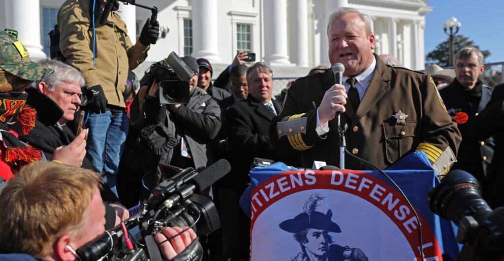 Culpeper County, Virginia, Sheriff Scott Jenkins in a brown uniform and surrounded by media speaks during a gun rights rally with the Virginia Capitol in the background