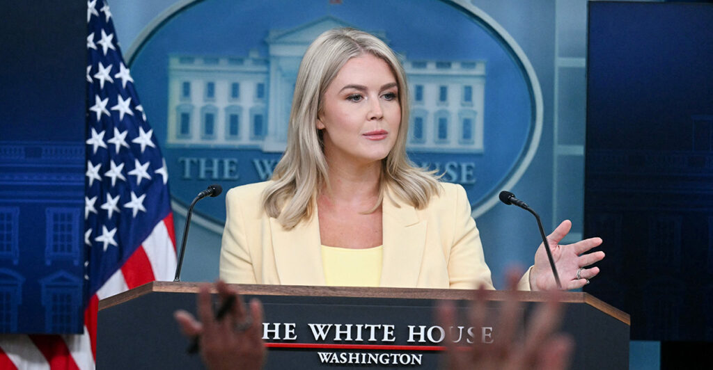 Karoline Leavitt in a yellow suit faces a question from behind the podium at a White House briefing.