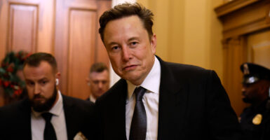 DOGE head Elon Musk in a black suit and tie walking through the halls of Congress