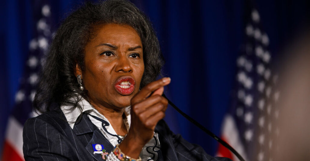 Virginia Lt. Gov. Winsome Earle-Sears speaks at a podium with American flags in the background and gestures by pointing her finger to the audience