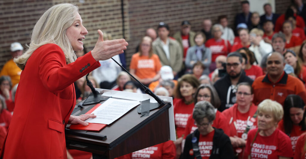 Virginia Democratic gubernatorial candidate Abigail Spanberger In a red suit speaks from the stage to a crowd of people mostly in red shirts at an anti-gun rally.