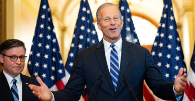 Mike Johnson stands next to John Thune, who has his arms spread wide. Behind the congressional leaders are four American flags.