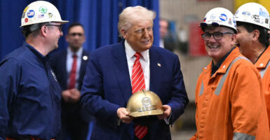 Donald Trump, gold hard hat in hand, jokes with three steel workers.