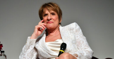 Actress Patti LuPone sitting in a white dress looking stern.