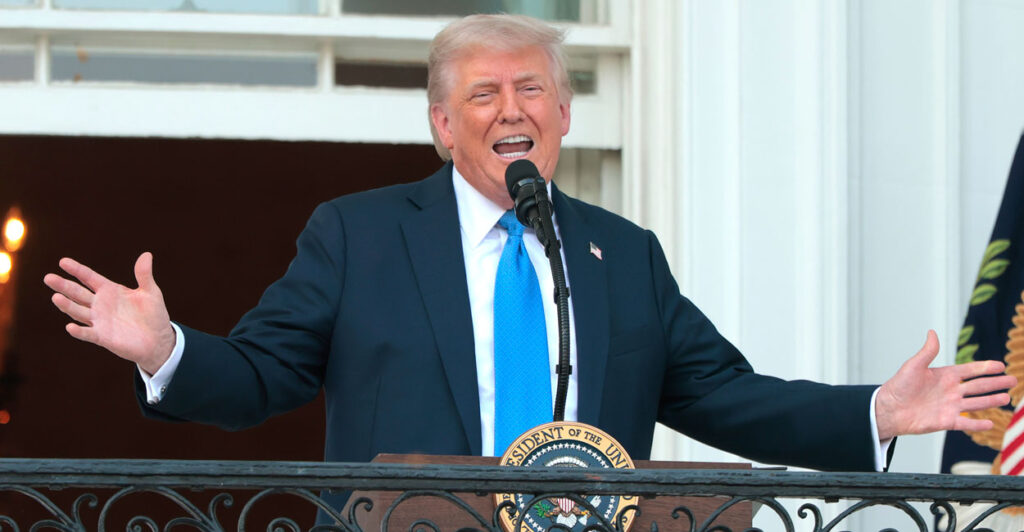 President Donald Trump, arms outstretched speaks from White House balcony.