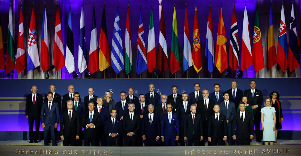 NATO leaders gather for a formal portrait underneath the flags of NATO nations.