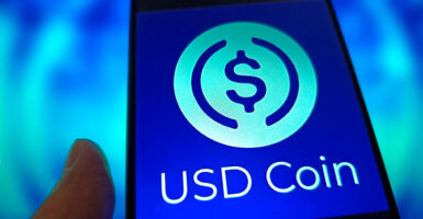 An illustration shows the USD Coin logo displayed on a smartphone.