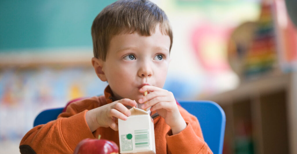 A young boy drinks from a single-serve carton of milk.