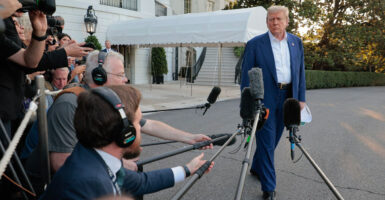 Donald Trump strolls past a group of reporters all pointing microphones at him.
