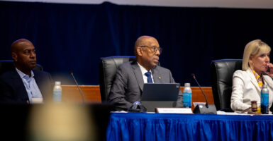 Michael Drake sits between two other University of California regents at a board meeting as he looks to his left.