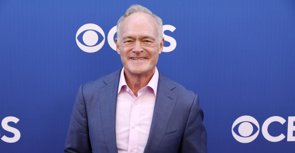 Scott Pelley stands with his hands at his side while he stands on the red carpet.