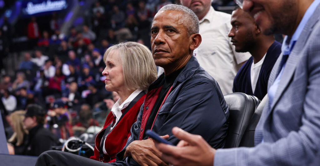 A stern looking former President Barack Obama, arms folded, attends the game between the LA Clippers and the Detroit Pistons at Intuit Dome on March 05, 2025 in Inglewood, California.