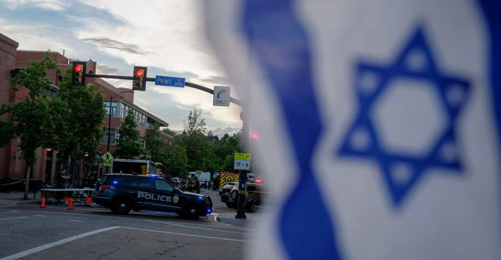 An Israeli flag seen flying with police cars in the background of a city street.