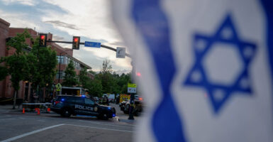 An Israeli flag seen flying with police cars in the background of a city street.