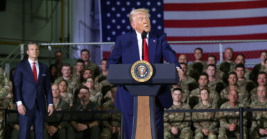 Donald Trump addresses Michigan Air National Guard Troops, with a bleacher of troops and an American flag behind him.
