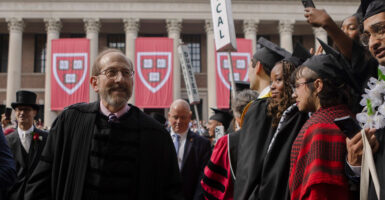 Alan Garber stands wearing a graduation gown and looks out at a crowd.