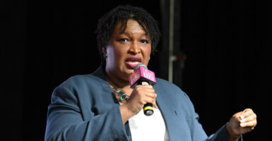Stacey Abrams stands with a microphone in her right hand as she speaks and looks to her right.