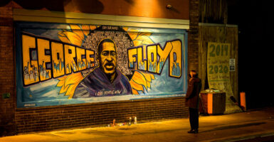 A man stands in front of a mural of George Floyd.