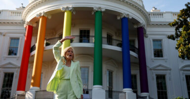 Jill Biden stands in front of the White House that has been decorated in rainbow colors while holding her right arm up in the air.