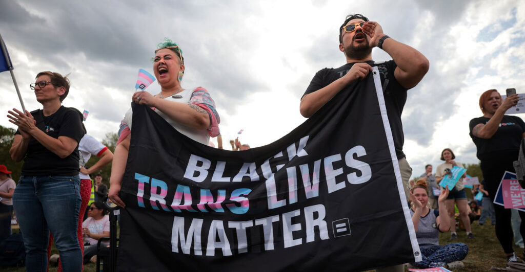 Two people hold up a sign that says, "Black Trans Lives Matter" at a rally.
