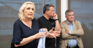 Marine Le Pen stands gesturing with her hands while talking to a crowd of reporters.