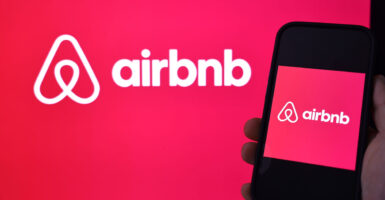 Airbnb logo against pink background on screen and on screen of smartphone.