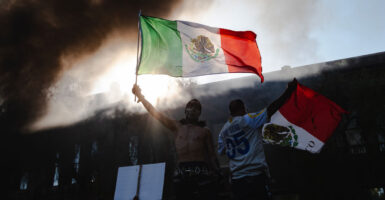 LA Riot. As smoke rises behind them protesters wave Mexican flags.