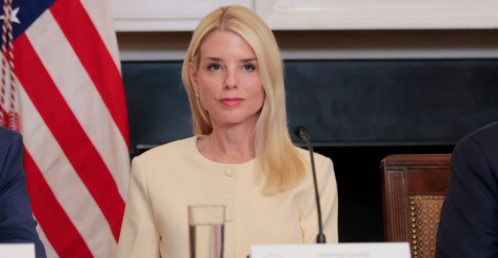 Attorney General Pam Bondi in a beige suit sits behind microphone.