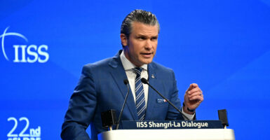Defense Secretary Pete Hegseth in a blue suit against a blue background makes a point at the Shangri La Dialogue Summit in Singapore.