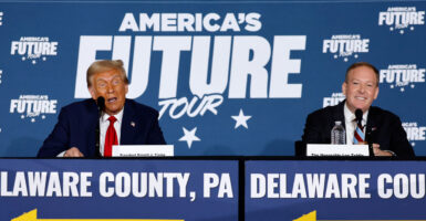 Donald Trump and Lee Zeldin sit together on a dias at a 2024 campaign event in front of sign reading "America's Future Tour."