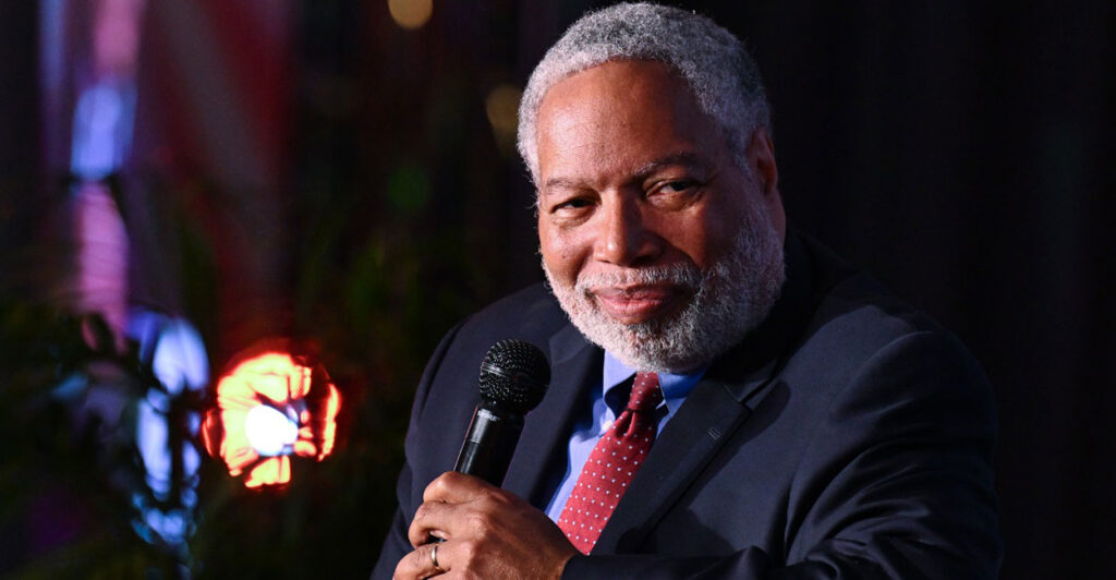 Lonnie Bunch sits while holding a microphone in his left hand as he turns his head to the left.