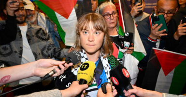 Greta Thunberg stands in a room surrounded my microphones put in front of her face.