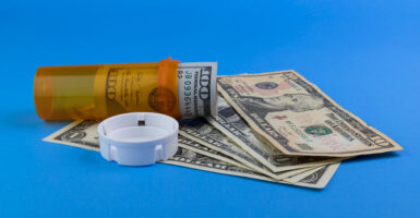 A roll of hundreds in a prescription bottle next to some more bills against a blue background.