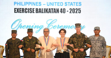 U.S. and Filipino military and civilian figures lock arms underneath "Exercise Balikatan 40-2025" banner.