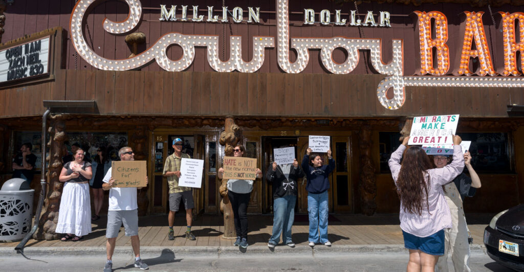 A small crowd gathers in front of the Million Dollar Cowboy Bar as part of No Kings Day protest.