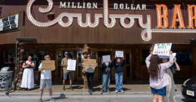 A small crowd gathers in front of the Million Dollar Cowboy Bar as part of No Kings Day protest.