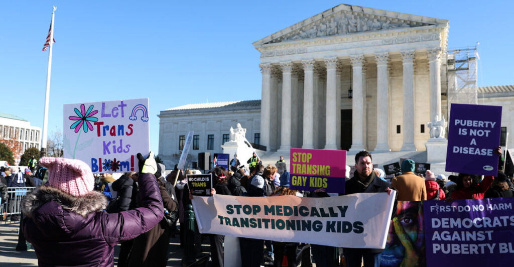 Demonstrators in support of a ban on "gender-affirming care" for minors stand in front of Supreme Court with signs and banners. One pro-gender-affirming care demonstrator faces them with her own sign reading "Let Trans Kids Bloom."