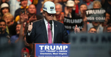 Donald Trump in a hard hat, giving two thumbs up at 2016 rally with coal workers.