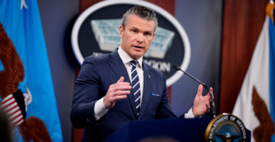 Pete Hegseth, arms spread, speaks from behind a podium to press at Pentagon briefing.