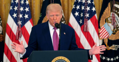 Donald Trump, arms spread behind a podium, with flags behind him.