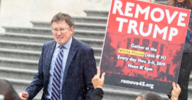 As rain falls, Thomas Massie stands on the Capitol steps while a protester holds up a "Remove Trump" sign.