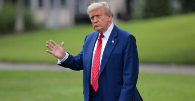 Donald Trump in a blue suit and red tie waves as he walks across White House lawn.