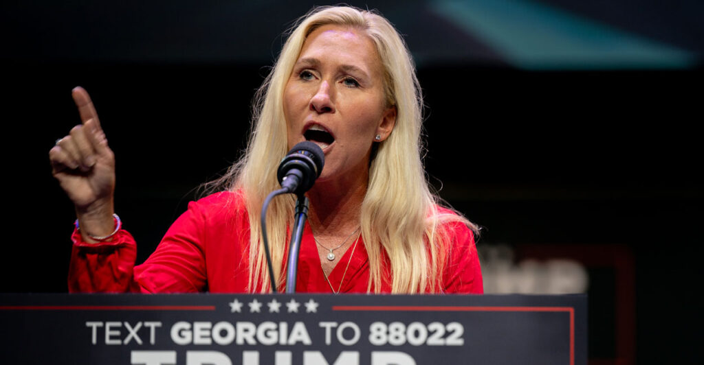 Rep. Marjorie Taylor Greene, R-Ga., in a red outfit and speaking at a Trump rally