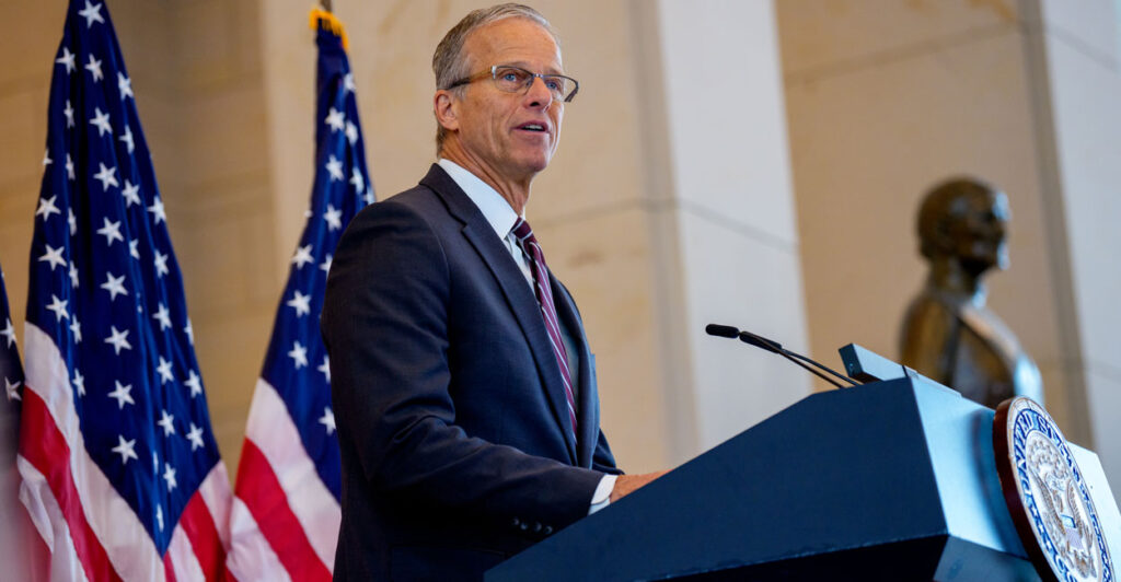 Sen. John Thune speaking at a podium, with two American flags behind him.