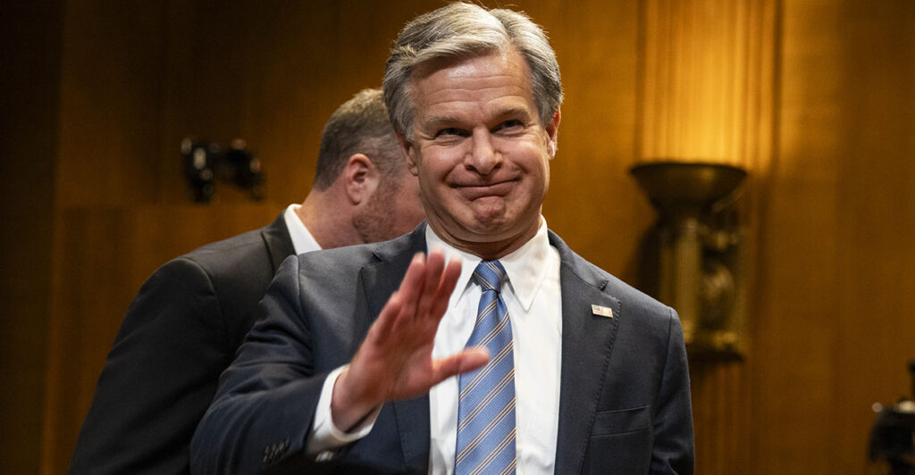 Christopher Wray in a suit waves