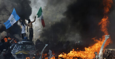 Two men wave the Mexican and Guatemalan flags amid burning cars during the LA riots.